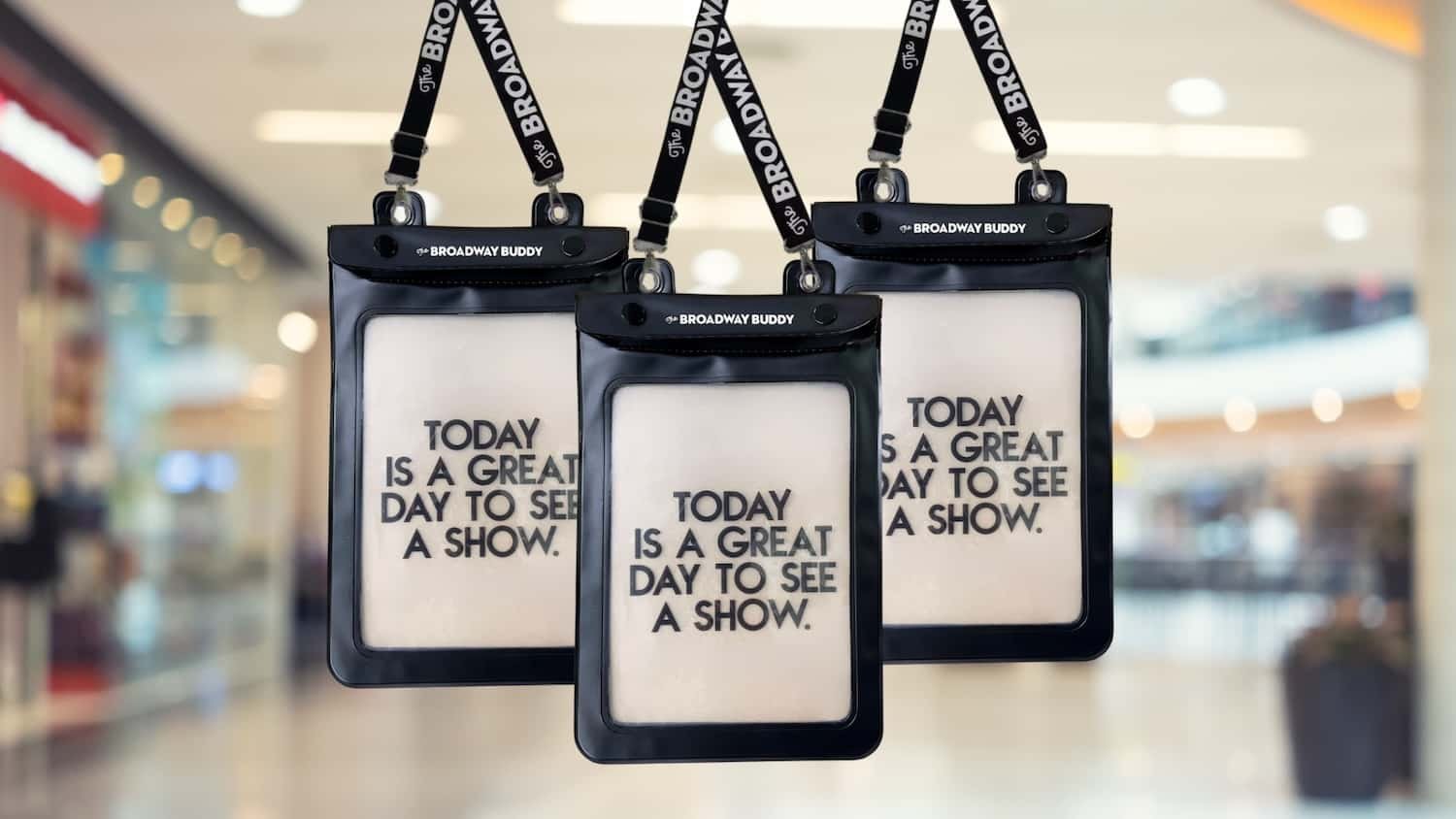 Three clear pouches with the message "Today is a great day to see a show" hanging from lanyards in a well-lit indoor setting.